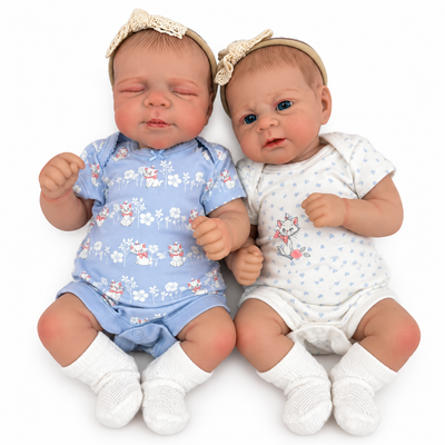 Two realistic reborn baby dolls lying side by side on a white background. The doll on the left wears a light blue floral short-sleeve bodysuit, white socks, and a beige lace headband.